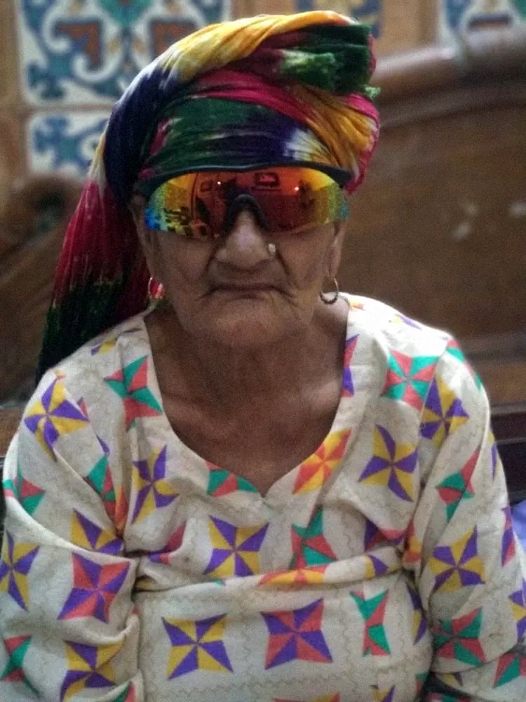 An older Egyptian woman in a colourful headscarf and mirrored sunglasses